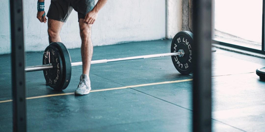 man in black t-shirt and black shorts holding black barbell
